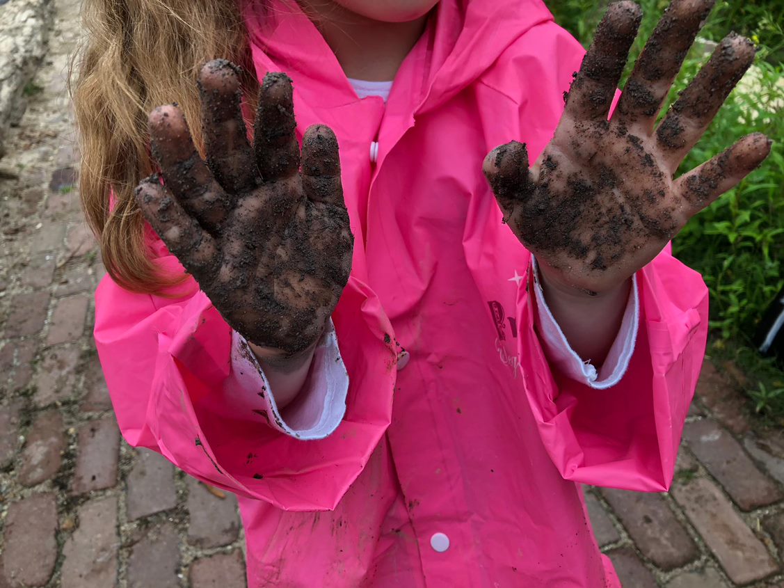 Meisje met modderhanden en roze regenjas